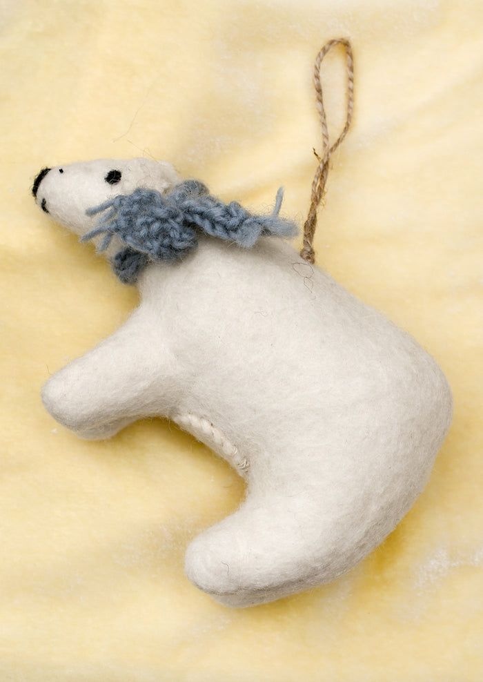 A white felt polar bear Christmas ornament with a knitted blue-gray scarf and a brown jute hanging loop.