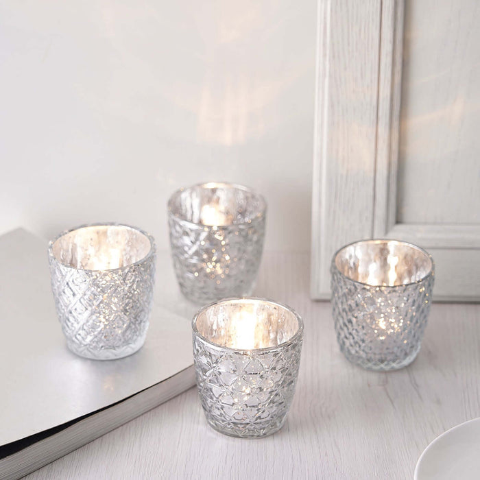 Set of four elegant glass candle holders with intricate patterns.