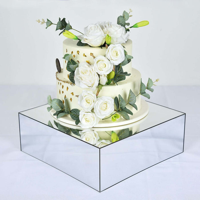 Elegant wedding cake adorned with white roses and greenery on a mirrored base.