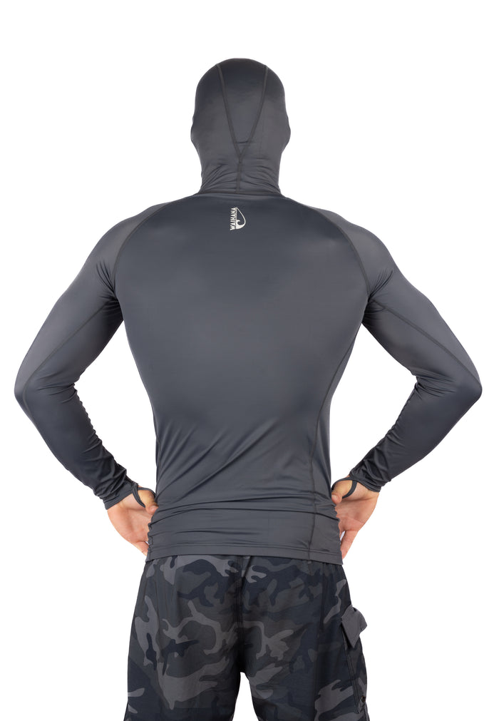 Back view of a male model wearing the Waihana Anthracite Carvico Hooded Surf Rashguard in dark grey with long sleeves and integrated hood, paired with dark camouflage shorts.