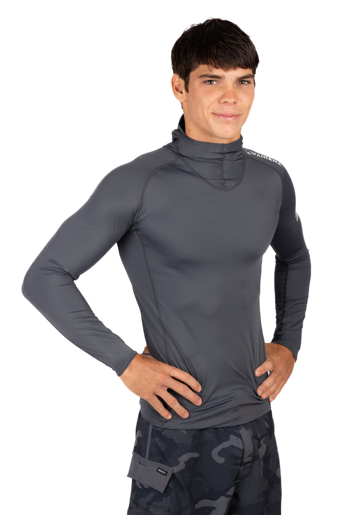 Male model wearing the Waihana Anthracite Carvico Hooded Surf Rashguard in grey with dark raglan sleeves and a built-in neck gaiter hood, hands on hips against a white background.