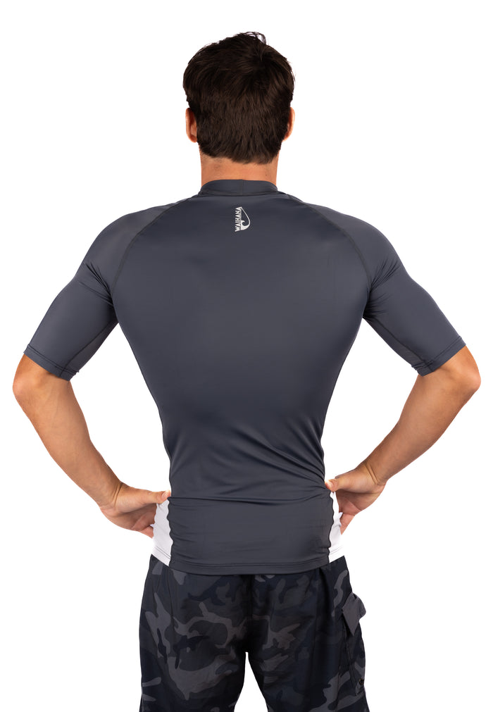 Back view of a male model wearing the Waihana Anthracite Short Sleeve Rashguard with white side panels and Waihana logo at the nape, paired with dark camo shorts on a white background.