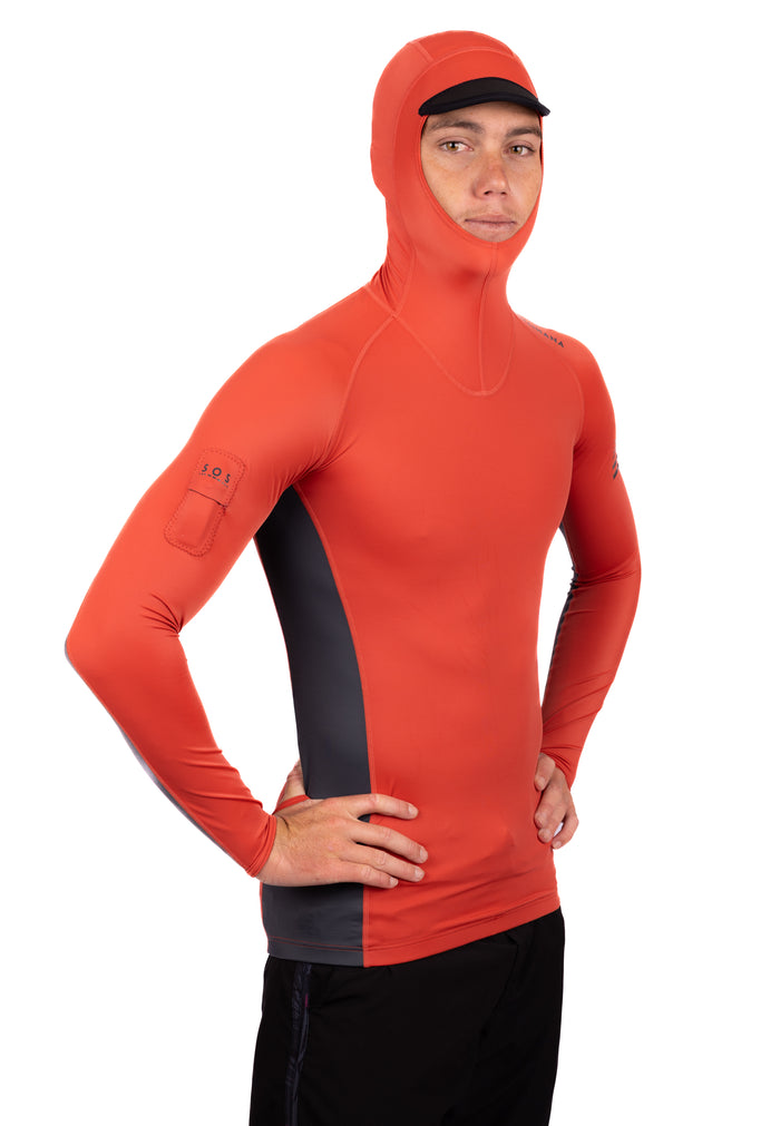 Male model wearing the Waihana Canyon Hooded Voyager Rashguard in orange-red with dark grey side panels and an integrated hood with black brim, hands on hips in a studio setting.