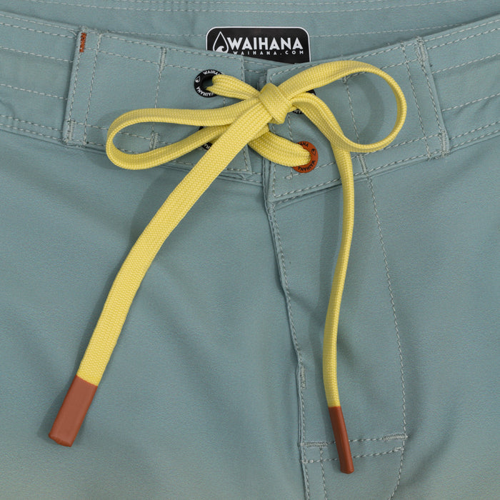 Close-up of the Waihana Dawn Patrol W1 Board Shorts waistband featuring a tied yellow drawcord with brown aglets, Waihana branded eyelet, and teal fabric with contrast stitching.