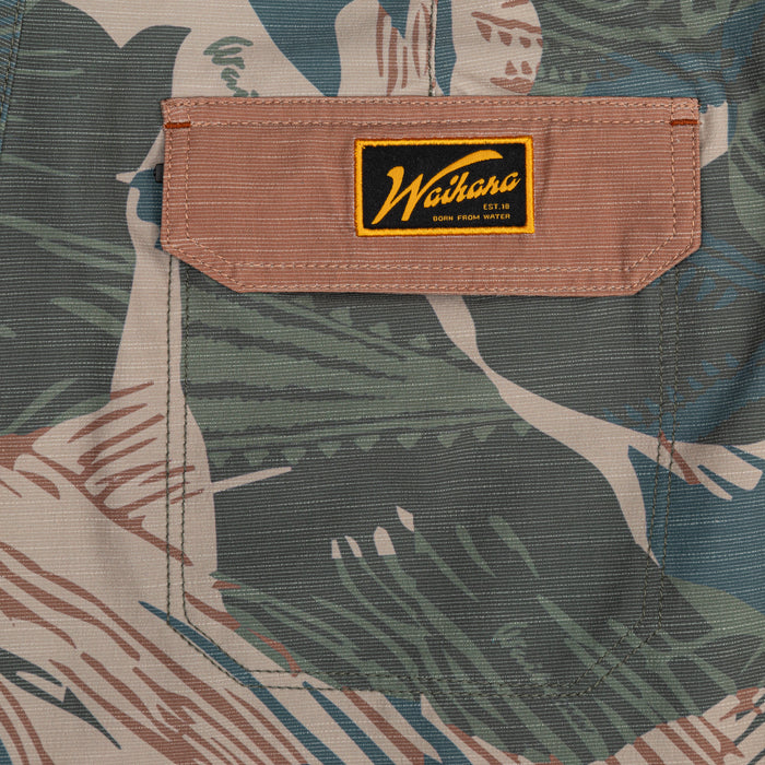 Close-up of the cargo pocket and embroidered Waihana 'Born From Water' label on the Hawaiian Brushstroke Cruiser board shorts in a tropical print fabric.