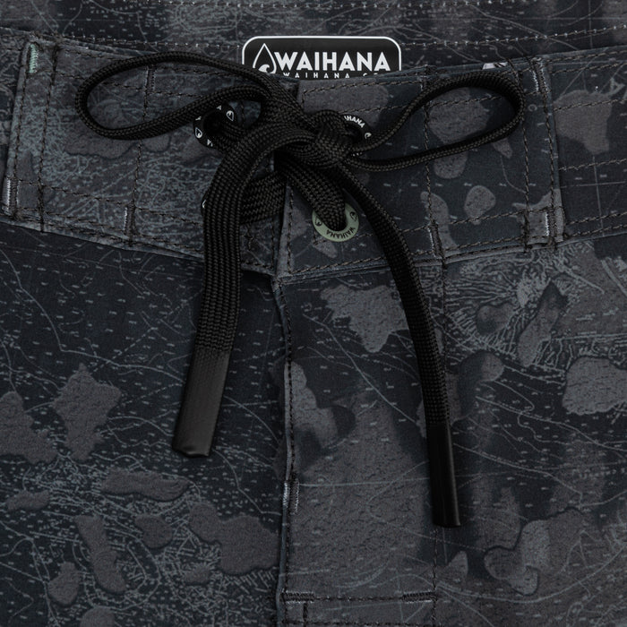 Close-up of the black drawstring waistband on Waihana Island Aloha W1 board shorts, showcasing the branded label, logo rivet, and dark cartographic camo print fabric.