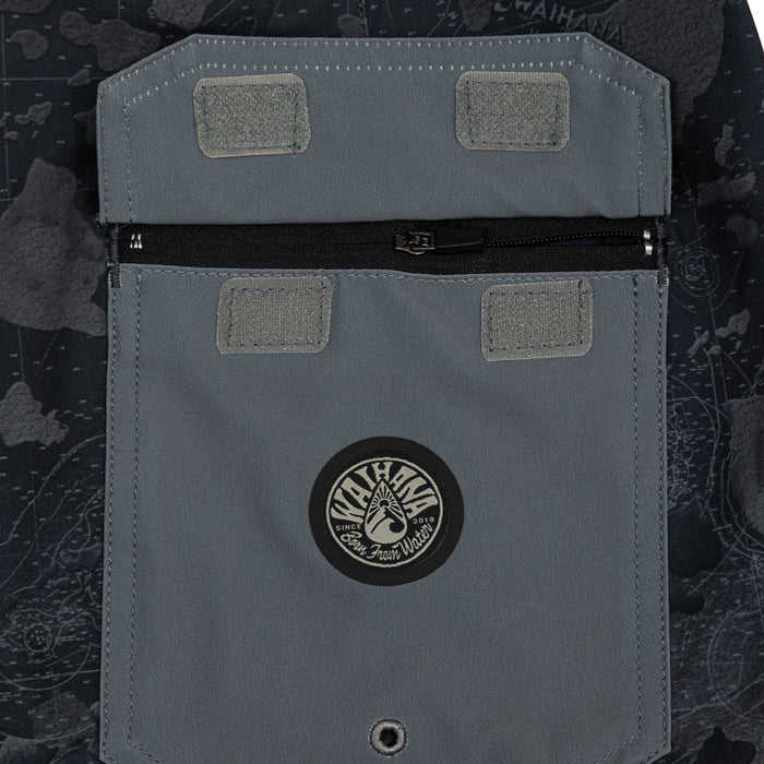 Close-up of the cargo pocket on Waihana Island Aloha W1 board shorts featuring a black zipper, velcro patches, and a circular Waihana Born From Water logo badge on dark nautical camo fabric.