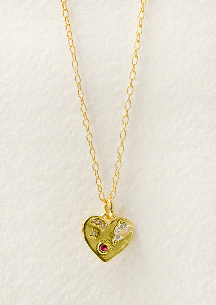 A gold necklace with a gold heart charm adorned with glass crystal and a red gemstone.
