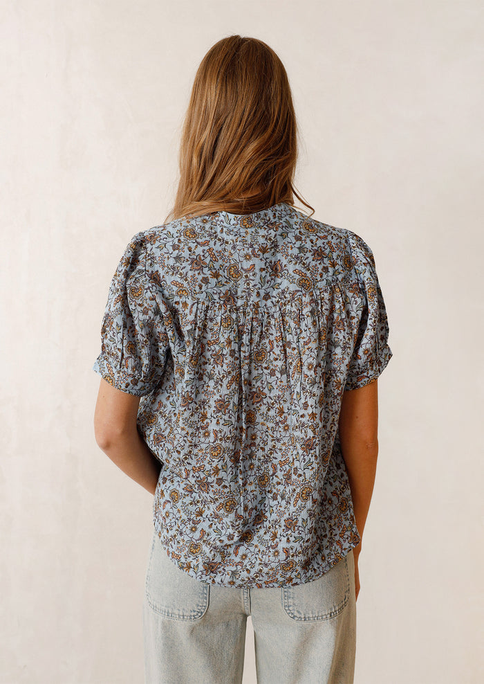 Woman wearing blue and brown printed top, seen from the back.
