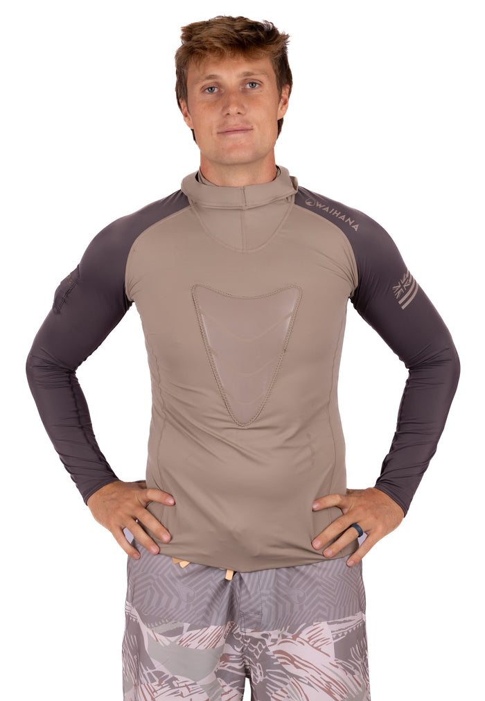 Male model wearing the Waihana Mana Hooded Spearfishing Rashguard in tan with dark grey contrast sleeves, featuring a chest panel and hood, paired with patterned board shorts, on a white background.