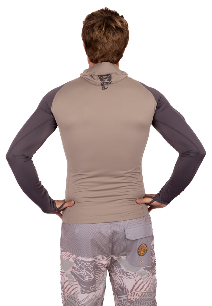 Back view of a male model wearing the Waihana Mana Hooded Spearfishing Rashguard in tan with dark grey sleeves and Waihana logo at the nape, paired with patterned board shorts.