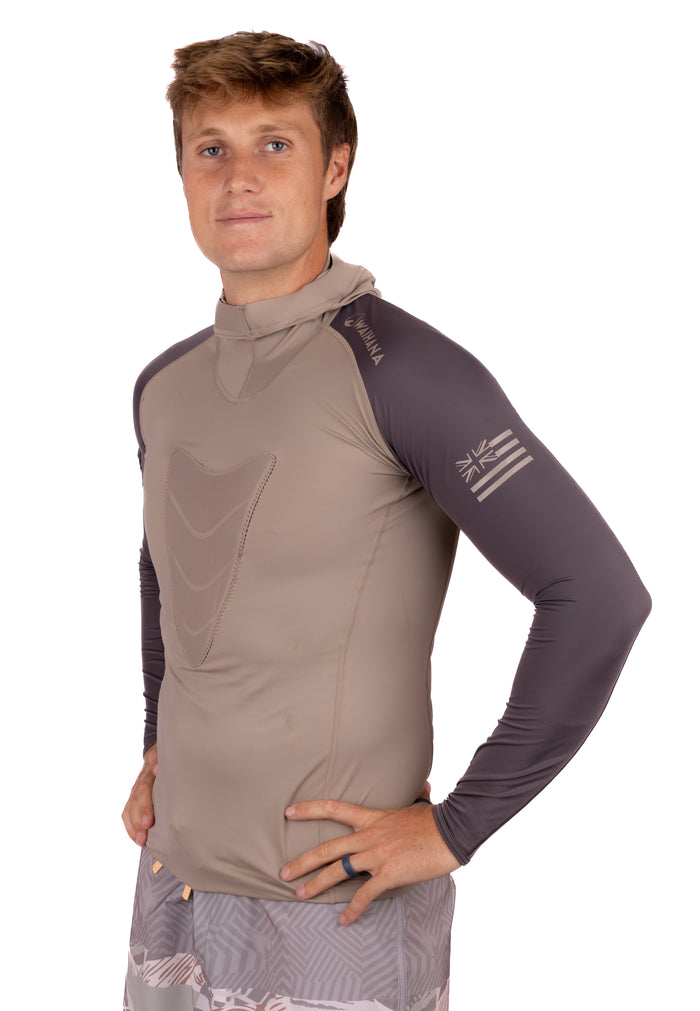 Male model wearing the Waihana Mana Hooded Spearfishing Rashguard in tan and dark gray with Hawaiian flag logo on the sleeve, photographed against a white studio background.