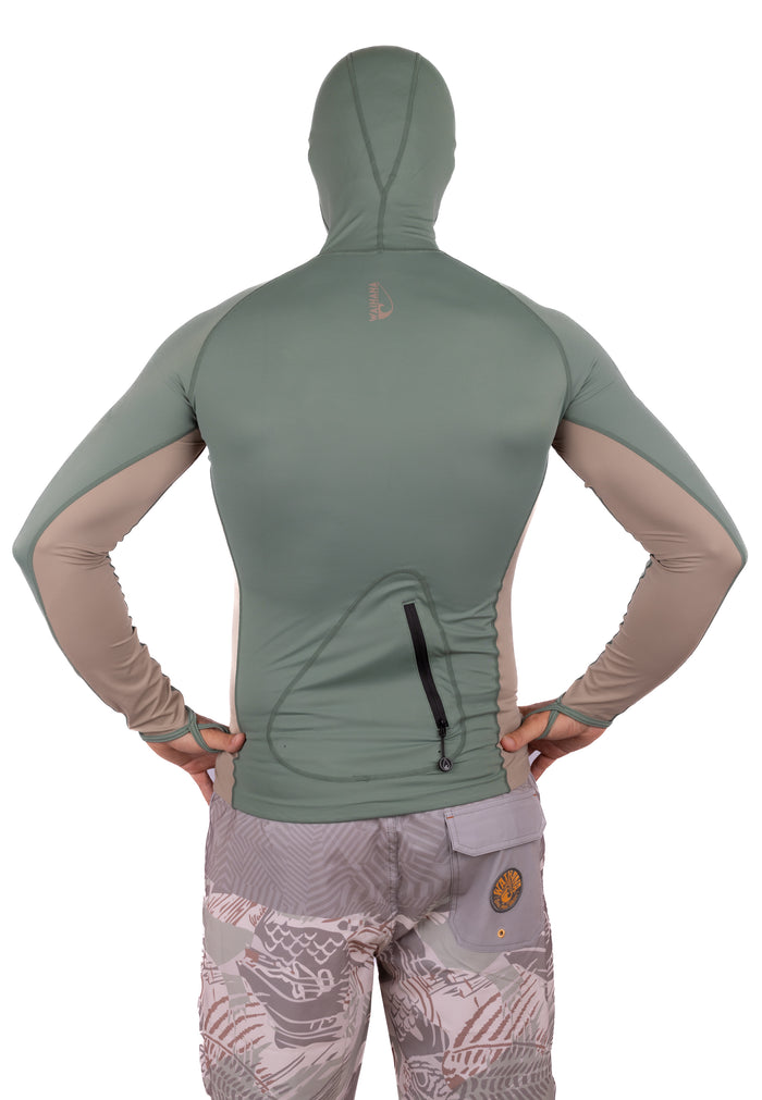 Back view of a male model wearing the Waihana Olive Hooded Voyager Rashguard featuring a sage green and tan two-tone design, full hood, long sleeves with thumb loops, and a zippered back pocket, styled with patterned board shorts.
