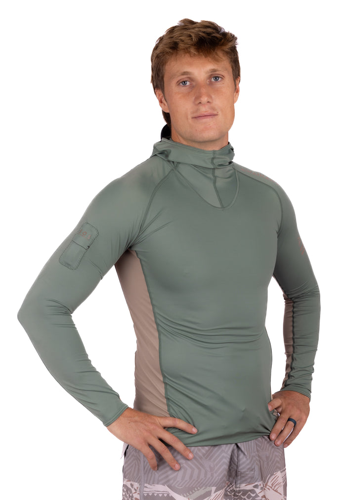 Male model wearing the Waihana Olive Hooded Voyager Rashguard, a long-sleeve olive green rashguard with tan side panels and built-in hood, shown from a slight angle against a white studio background.