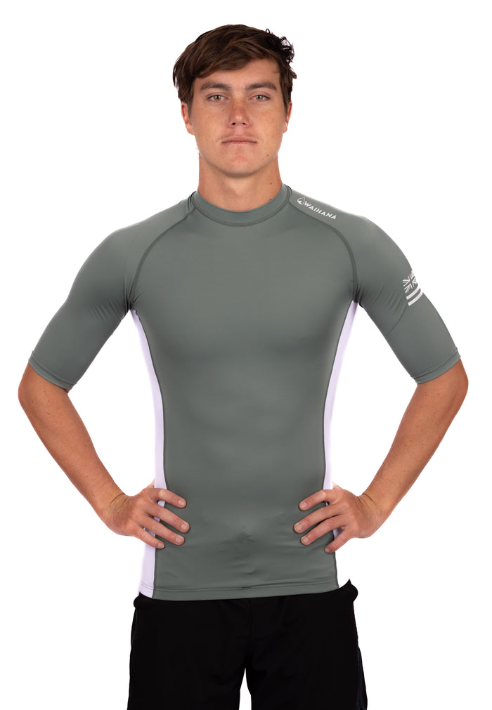 Male model wearing the Waihana Olive Short Sleeve Rashguard with white side panels and Hawaiian flag logo on the sleeve, shown from the front against a white background.