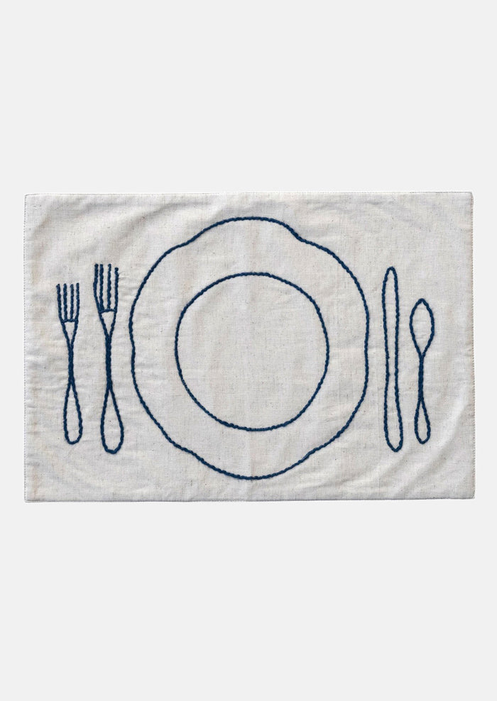 An off-white linen-cotton placemat with navy blue plate and silverware embroidery.