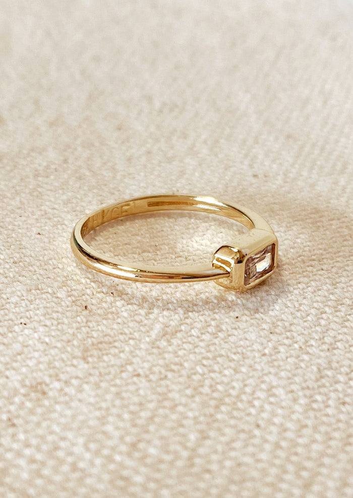A gold ring with single rectangular clear stone.