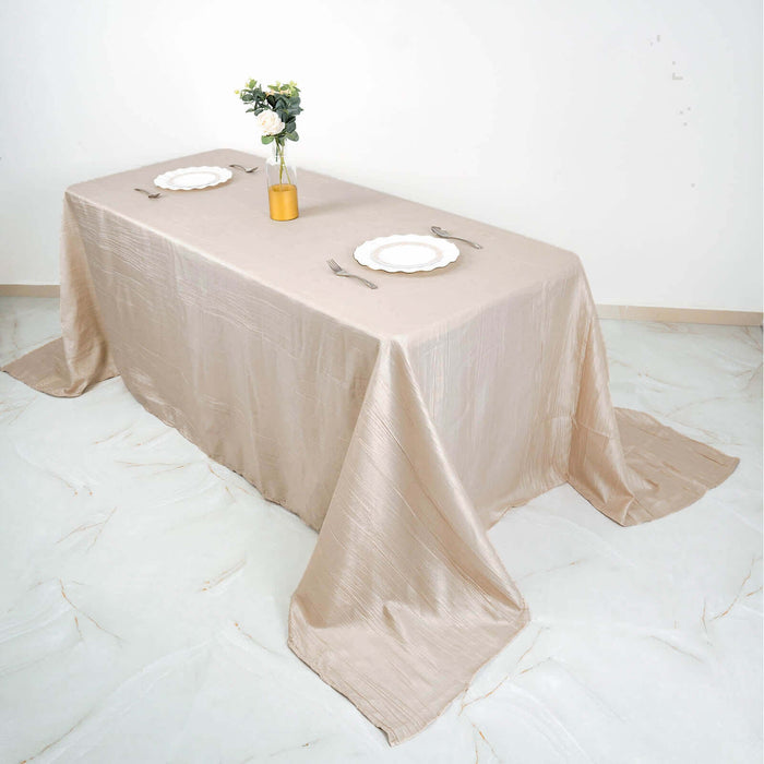 Elegant beige tablecloth draped over a dining table with plates and a flower vase.