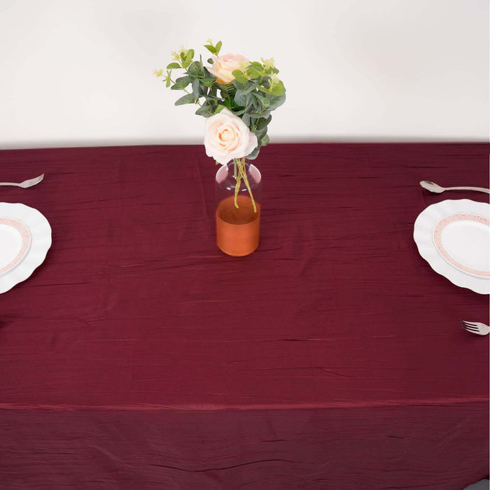 Table setting with burgundy tablecloth, plates, and a vase of roses.