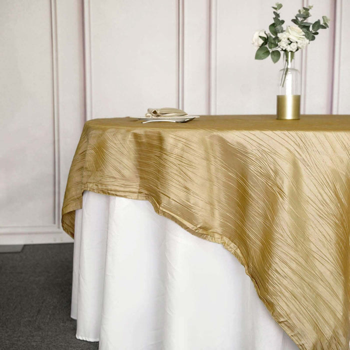 Gold textured tablecloth draped over a white table with a vase of flowers.