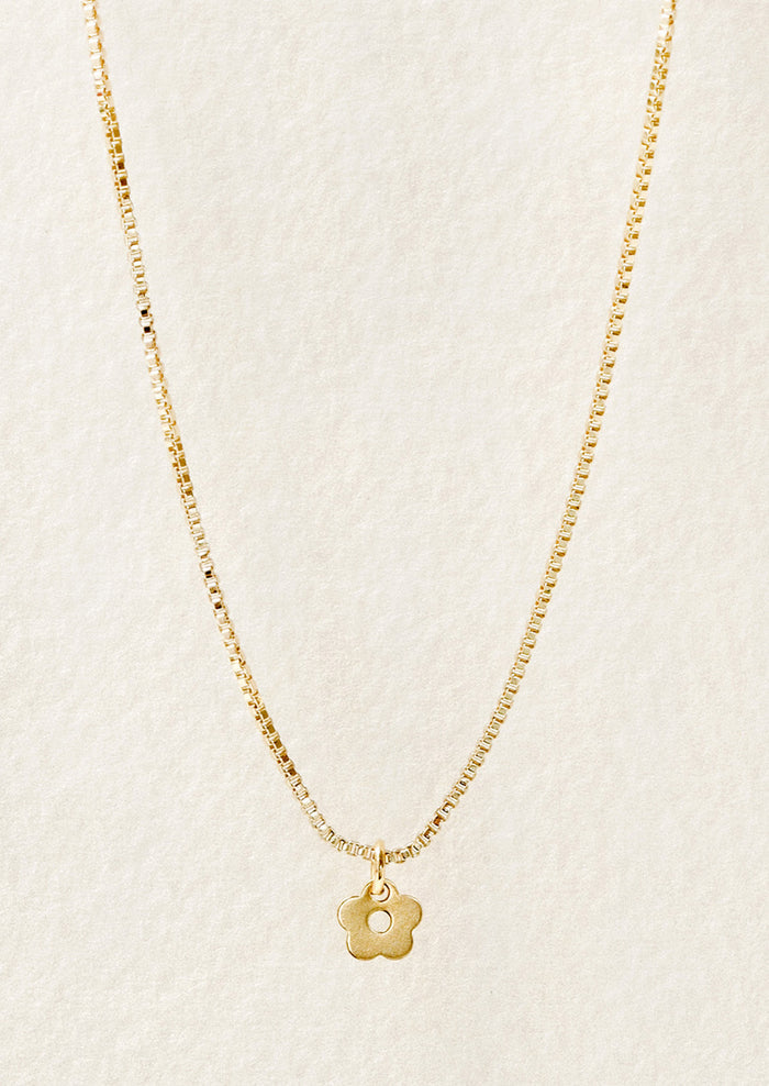 A gold chain necklace with a tiny daisy charm in front of a white background.