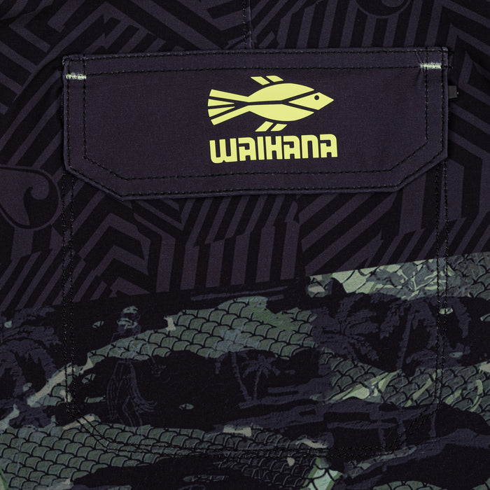 Close-up of Waihana Tropicam W1 board shorts pocket flap featuring the yellow Waihana fish logo on dark fabric with a geometric tribal pattern and green camo fish-scale print.