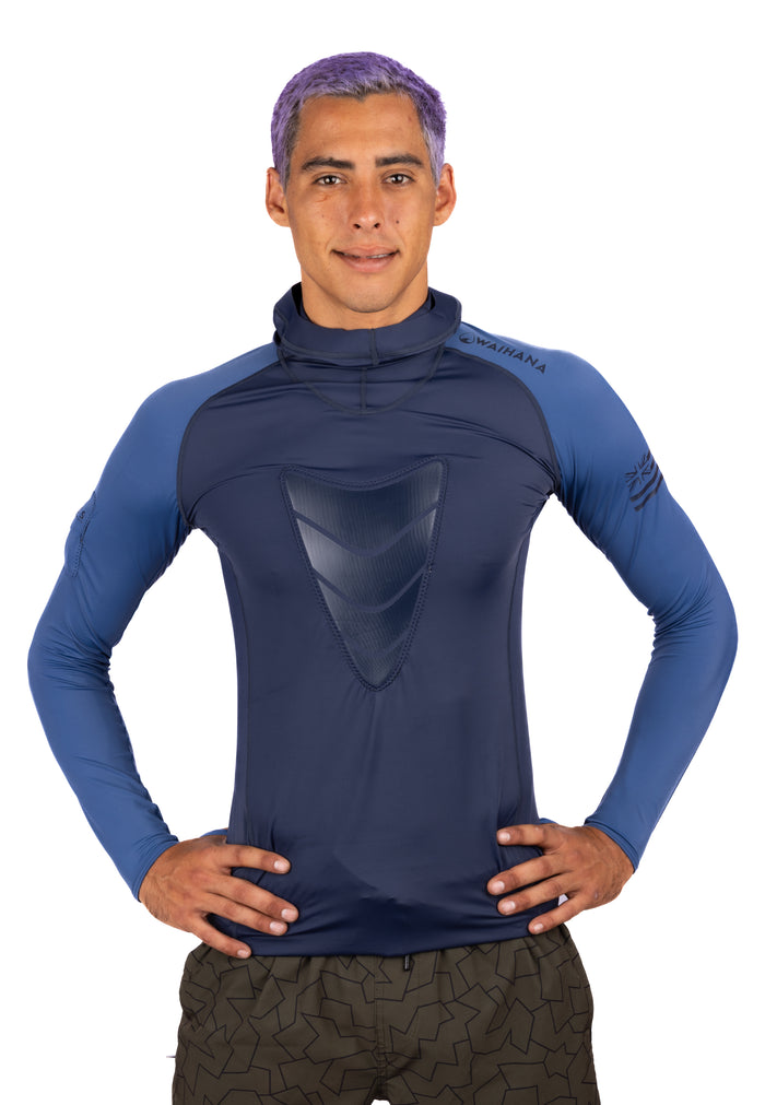 Male model with purple hair wearing the Waihana Vista Hooded Spearfishing Rashguard in a two-tone navy and blue colorway, featuring a molded chest panel and zip-up hood, paired with dark board shorts.