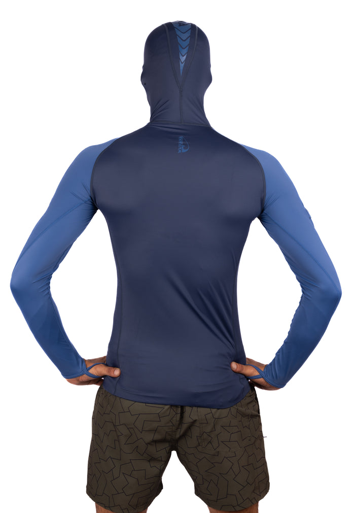 Back view of a male model wearing the Waihana Vista Hooded Spearfishing Rashguard in navy and blue two-tone long-sleeve design with integrated face hood and thumb loops, paired with patterned board shorts.