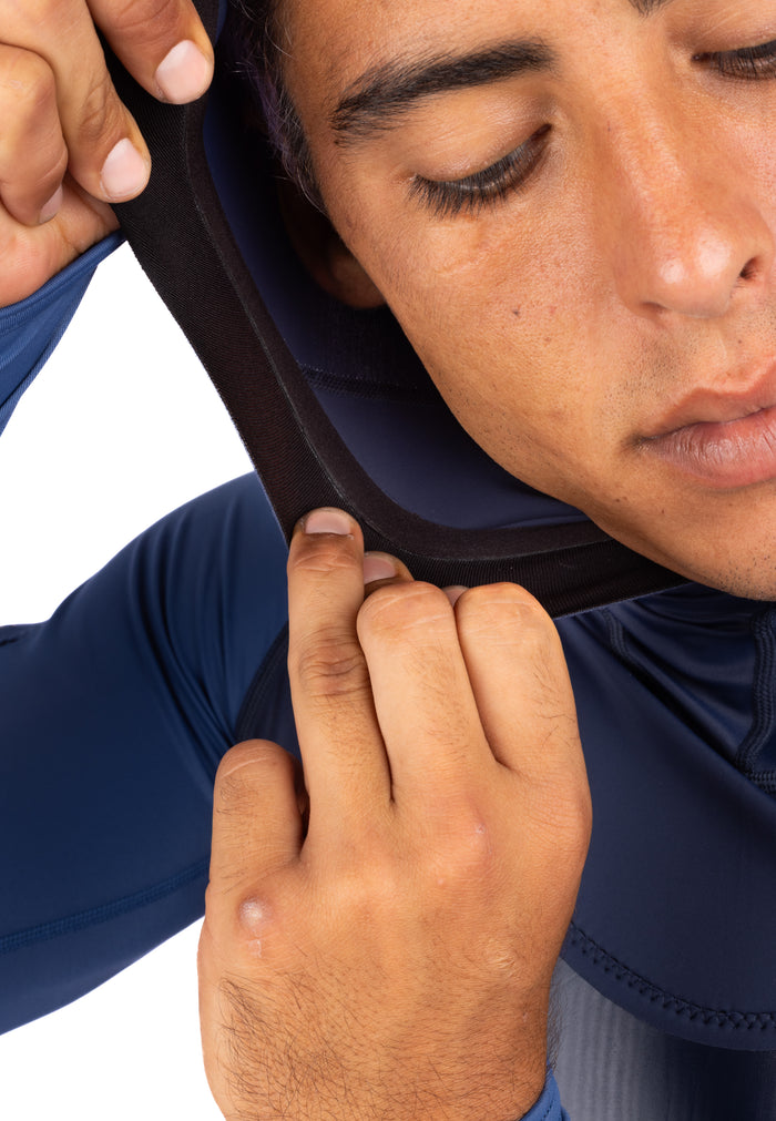Close-up of a man adjusting the neoprene-lined hood opening of the Waihana Vista Hooded Spearfishing Rashguard in navy blue.