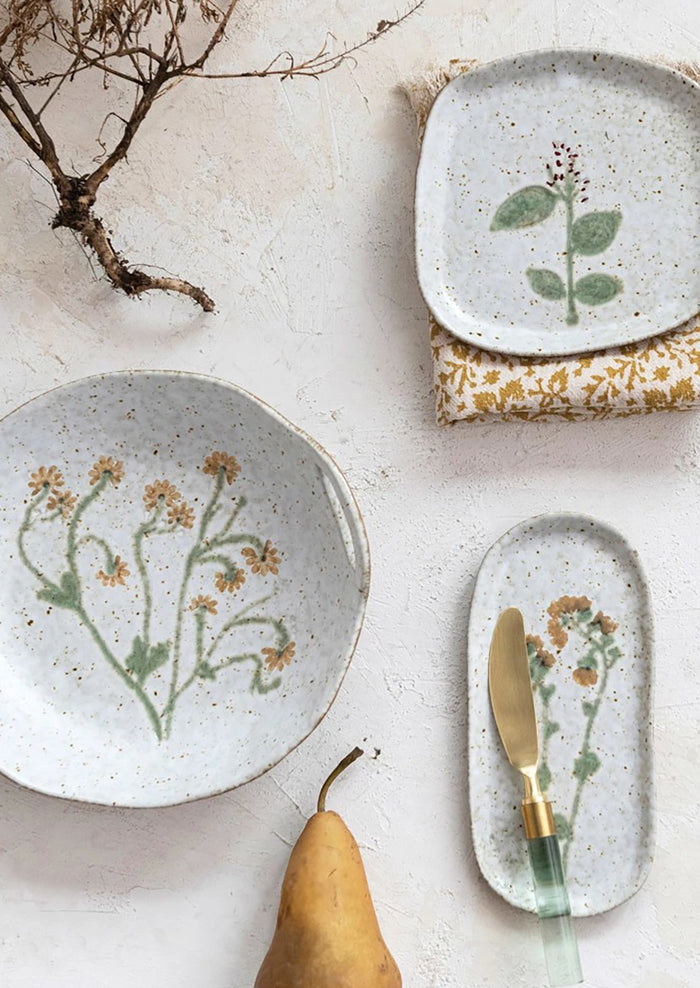 A ceramic serving bowl with cutout side handles and yellow painted flower at center.